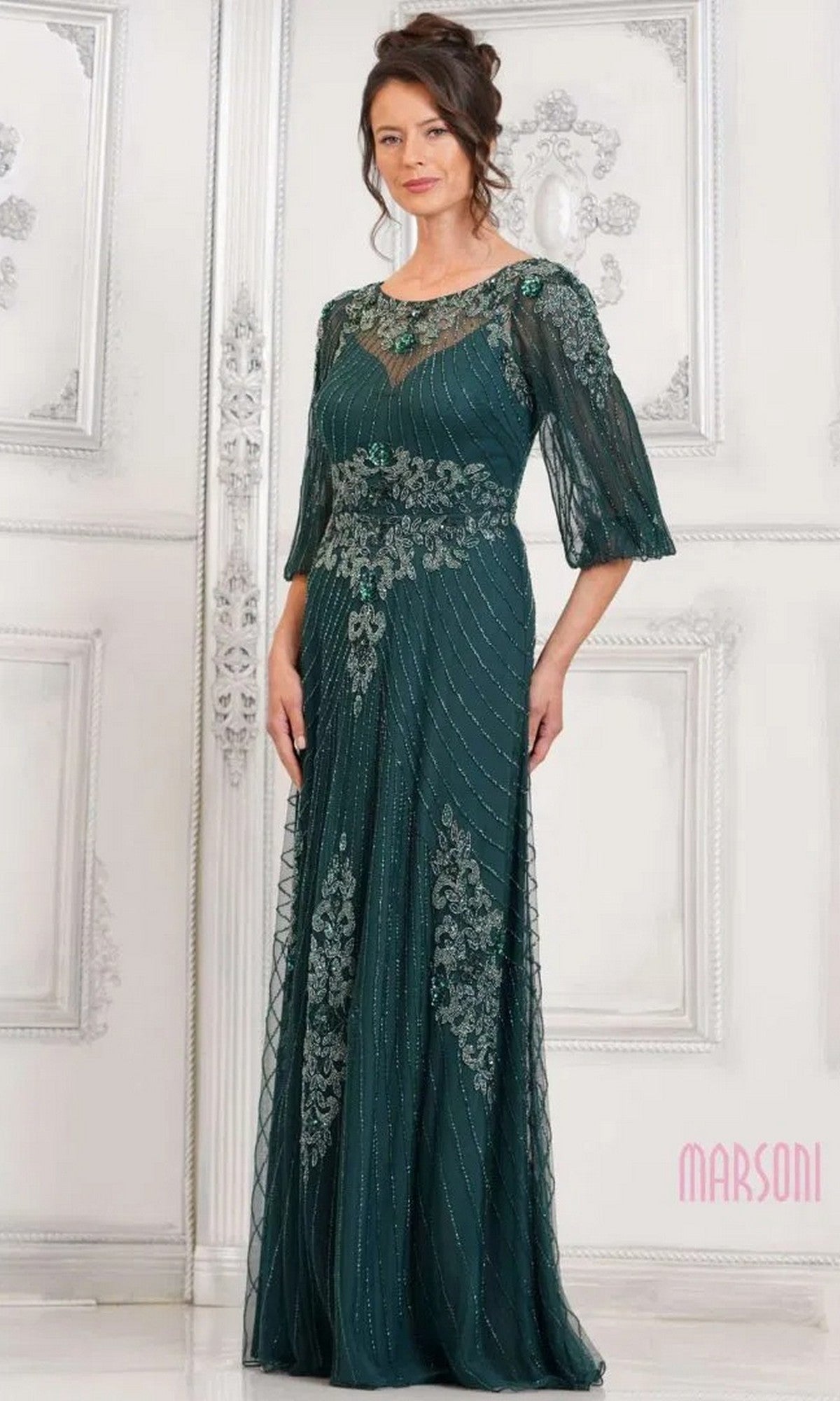 A woman wearing the Marsoni MV1323 long formal dress, featuring elegant beaded mesh and lace embellishments, stands in a white ornate room.